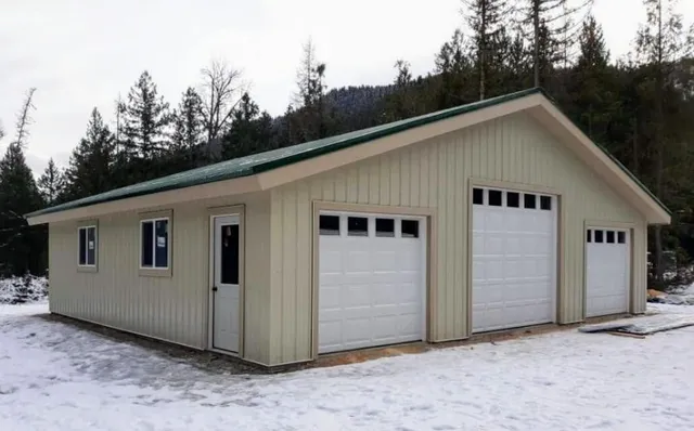 A garage with three garage doors and a green roof in the snow.