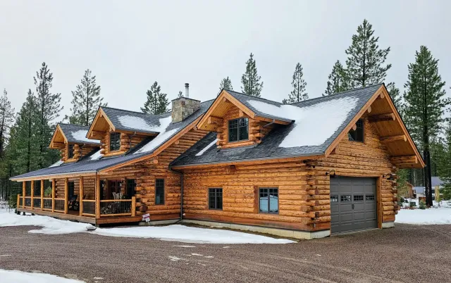 A large log cabin with a garage and porch in the snow.