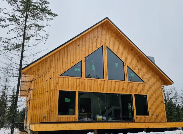 A large wooden house with a lot of windows is surrounded by snow.